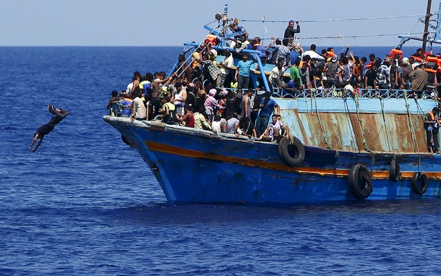 A+migrant+dives+into+the+water+from+an+overloaded+wooden+boat+during+a+rescue+operation+10.5+miles+off+the+coast+of+Libya